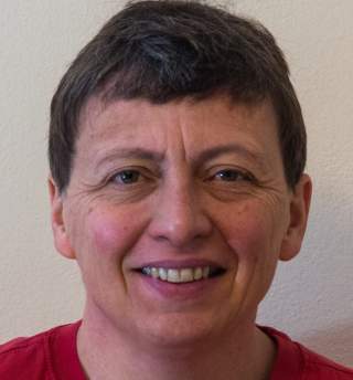 Porträt einer lächelnden Person mit kurzen braunen Haaren vor hellgrauem Hintergrund.
