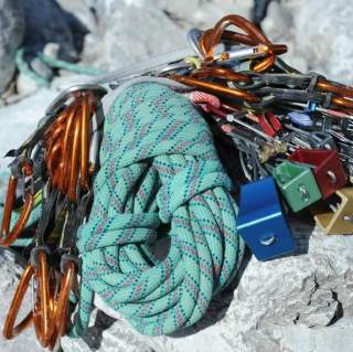 Kletterausrüstung bestehend aus einem zusammengerollten Seil, mehreren Karabinern und bunten Sicherungsgeräten liegt auf Felsen.