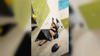 Eine junge Frau klettert in einer Boulderhalle an einer steilen Kletterwand mit verschiedenen bunten Griffen.
