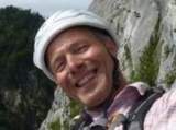 Mann mit weißem Hut lächelt vor einer felsigen Berglandschaft.