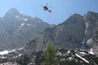 Helikopter in den Bergen im Rettungseinsatz, eine Person wird mit einer Seilwinde geborgen.