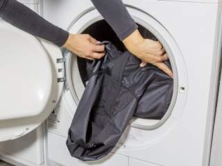 Eine Person legt ein schwarzes Kleidungsstück in eine offene Frontlader-Waschmaschine.