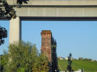 Ein Sandsteinpfeiler unter einer Stahlbetonbrücke, daran klettert ein Mann. Im Hintergrund einige Häuser über einem Weinberg.