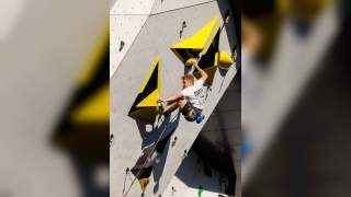 Ein Mann klettert an einer Kletterwand mit großen gelben und schwarzen Griffen, gesichert durch ein Seil.