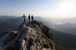Zwei Wandernde erreichen das Gipfelkreuz.