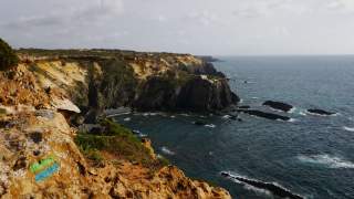 Felsige Küste mit steilen Klippen und markiertem Wanderweg am Meer unter bewölktem Himmel.