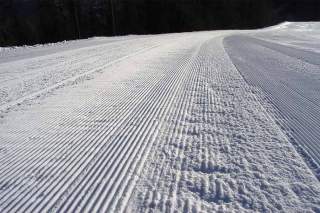 Nahaufnahme einer frisch gespurten und geglätteten Skipiste mit parallelen Linien im Schnee.