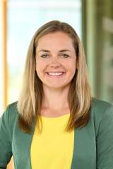 Sophie Hufnagl ist Referentin im Marketing Team des deutschen Alpenvereins. Sie trägt eine grüne Jacke, ein gelbes T-Shirt und lächelt. Sie steht im Treppenhaus der Bundesgeschäftsstelle. Das DAV Logo ist im Hintergrund.