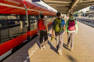 Drei Menschen mit Wandersachen laufen auf Bahngleis entlang